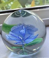 Clear image showing the glass paperweight with a blue flower and green leaves encased inside a spherical orb.