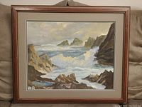 Framed painting depicting a rocky coastline with crashing waves, showing entire artwork, frame, and matting.