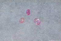 Three small oval pink sapphire gemstones on a gray textured background.