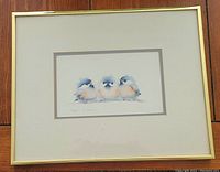 Framed print showing three bluebirds sitting together, matted and framed in gold with wooden floor background.