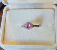 Close-up front view of the silver ring with pink gemstone set in prong claws, displayed in white padded ring box.
