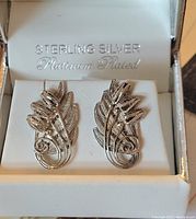 Pair of sterling silver platinum plated earrings displayed in an open white jewelry box with silver text showing "Sterling Silver Platinum Plated".