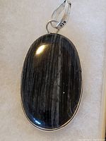 Close-up of the pendant showing the oval shape stone with dark and light gray stripes set in a .925 sterling silver bezel and bail.