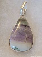 Close-up image of a teardrop-shaped stone pendant with purple, white, and green hues, set in sterling silver with a bail.
