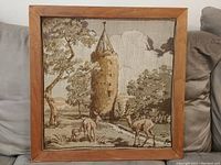 Front view of framed vintage textile stitching depicting deer near a tower.