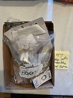 Box containing a variety of broken and mismatched jewelry pieces in plastic bags labeled for craft or repair.