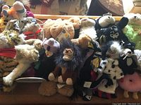 Overview of various collectible stuffed animals including Disney characters and others packed together on a bench showing variety of sizes and colors.