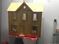 Front full view of the unfinished wooden dollhouse showing its shape, window set-up, and decorative scalloped trim near roof peak.