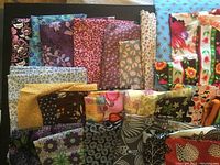 Various pieces of fabric stacked and folded showing different floral and patterned designs in dark and bright shades