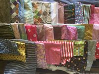 Photo shows large array of folded cotton fabric pieces laid out in rows, with various patterns including polka dots, stripes, checks, and plaids in multiple colors.