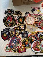 Photo showing various embroidered fire department patches from locations including Welland Fire Dept, City of Toronto Fire Department, North York Fire, Ambulance Brant County, Guelph Fire Dept, Baltimore, Los Angeles, Fire Dept of City of New York and others.