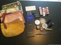 Photo showing unused makeup products including multiple cosmetic bags and assorted makeup items such as lipsticks, powders, mascara, and eye shadows.