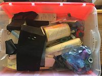 Sewing notions and fabric pieces inside a plastic container with an orange lid showing various items packed together