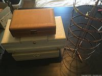 Side angle view showing stacked brown leather-like jewelry box, white jewelry boxes, and nearby circular metal earring stand.