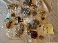 Image showing multiple plastic bags containing different strands of costume jewelry necklaces in assorted colors and styles on a fabric surface.