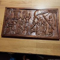 Front side of the African wood carving storyboard panel showing carved human figures and huts.