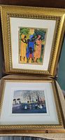 Two framed prints stacked in a chair, showing colorful figures and a scenic view.