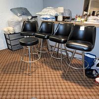 One backless stool at left, four stools with curved backrests at right, black vinyl seats, chrome legs