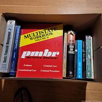 Top-down view of a cardboard box containing 9 books of various sizes and genres including law, finance and literature.