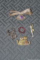 Five assorted brooch pins arranged on a textured gray background from the front view.
