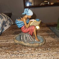 Side view of the life-like figurine showing woman seated, detailed clothing and basket contents.