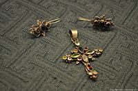 Photo showing colorful stone cross pendant and three pairs of earrings with various colored stones and gold-tone metal on textured fabric.