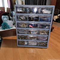 Multi-drawer organizer bin showing 24 small drawers with varied jewelry making supplies including beads, cords, and metal components in each drawer.