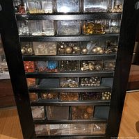 Front view showing multiple small compartments filled with a variety of beads and jewelry making supplies, sorted by type and color in a black organizer.