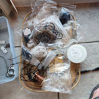 Basket containing assorted spools and bundles of jewelry making wires and cords including copper wire, leather cords, white thread, and other metal wires.
