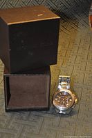 Michael Kors black watch box standing open next to the wristwatch on patterned fabric.