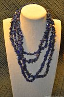Full view of two layered natural lapis lazuli necklaces displayed hanging on beige fabric bust stand against a textured dark background.