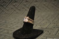 Photo of CZ wedding or engagement ring with a large square-cut stone on a black ring stand showcasing the front and side detail of the ring.