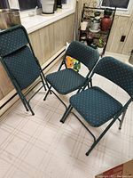 Three of the pine green padded Samsonite folding chairs, two set up and one folded showing seat and back upholstery pattern