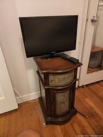 Samsung 19-inch TV on top of a decorative wooden side cabinet with floral painted drawer and door.