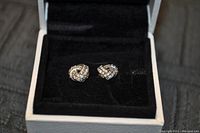 Close-up of the pair of Love Knot silver stud earrings with sparkling stones in a black velvet box.