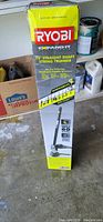 Photo of Ryobi 18 inch straight shaft string trimmer in original box standing upright in garage setting.