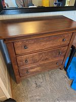 Front view of the solid wood brown dresser with three drawers, showing wood grain and black round knobs.