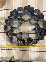 Round metal art piece with multiple tubes arranged concentrically on a fabric surface, measuring about 14 inches in diameter