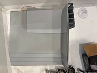 Grey metal bookends, one large and one small, placed on a shelf surface with suction cup and other small items nearby.