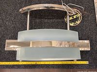 Top view of ceiling light fixture showing curved frosted glass panel and chrome metal bars. Wiring and mounting bracket visible.