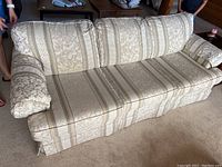 Photo of beige floral and striped upholstered couch with rolled arms and three back cushions, placed on carpeted floor with people standing nearby