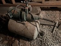 Metal jet pump and pressure tank resting on gravel floor in crawlspace