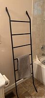 Black standing towel rack leaning against bathroom wall with a towel hanging on it.