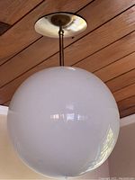 Close-up of a white glass globe light fixture mounted on a wood-paneled ceiling with brass-colored hardware.