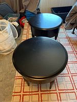 Two black round side tables with solid wood construction, photographed from above and slightly angled side view showing turned legs and worn surface.