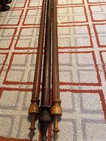 Three solid wood rods laid side by side showing turned finials in light and dark finishes