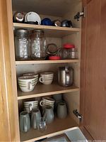 Kitchen cabinet shelf with glass mason jars, ceramic mugs, glass cups, and metal container
