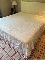 King-size bed made with a white cotton duvet cover and a white bed skirt with ruffled edges visible at the base of the bed.