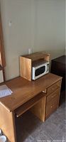 Wooden desk showing the upper shelf holding a microwave (microwave not included), slide-out keyboard tray, and pedestal drawers