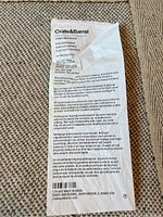 Close-up photo of the care and material label showing Crate & Barrel brand, 100% New Wool material, care instructions, and dimensions 8'x10'. Made in India.